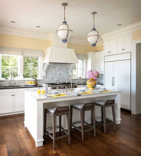 The custom Hull pendants from Urban Electric Company and Mattaliano Fente counter stools from Terris Draheim pair with existing white oak flooring. Benjamin Moore Simply White trim with Calming Cream walls complement the Sub-Zero refrigerator and Wolf range.