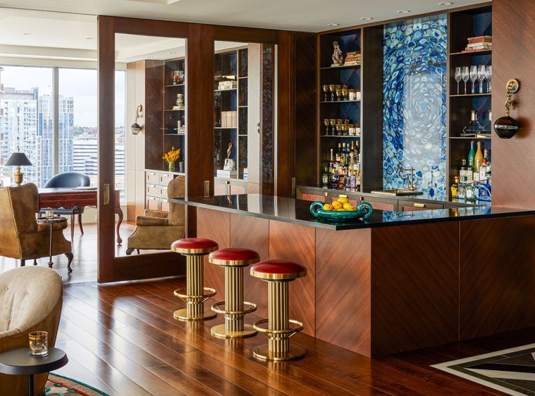 Art Deco stools from J Garner Home by J. Alexander face The Stone Collection’s backlit Blue Agate Slab. Harriet Industries antiqued brass countertops and shelves. Custom door and Fumed Oak casework with Brass Metal Screed details and leather panels by Stusser Woodworks.