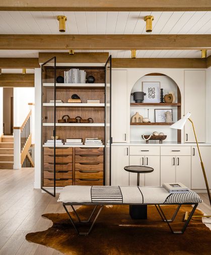 Initially surrounded by craftsman-esque built-ins, this area of the great room felt heavy and uninviting. Scherie replaced them with custom cabinetry by DMC Cabinets, including an arched vestibule and glass-fronted shelving matching the kitchen.