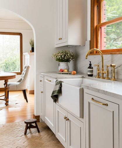 The custom cabinets by Acorn Cabinets feature Massey Unlacquered Brass hardware from Rejuvenation. They’re painted in Benjamin Moore Bruton White, a subtle, warm white with grey and beige undertones. Additional cabinets were added in the existing dining room to tie the spaces together. The Italian brass faucet and side spray are Rohl San Julio Bridge from Ferguson. The Classic Shaker Single Bowl Farmhouse Apron Front Fireclay Kitchen Sink is by Shaws and also sourced from Ferguson.