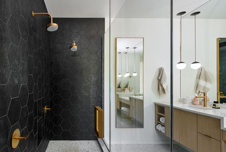 Creating a welcoming bathroom; textured Merola wall tile from Gaudi Hex, Calacatta Gold Honed Marble Penny Rounds from Tilez, brushed brass plumbing from Newport Brass, and Cedar and Moss pendant lighting.