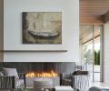 Artwork by Betsy Eby adorns the soaring fireplace with Twisted Metalworks fireplace surround and Bianco Mundra Quartzite slab from Architectural Stone Werkes. Holly Hunt Carpo Club swivel chairs.