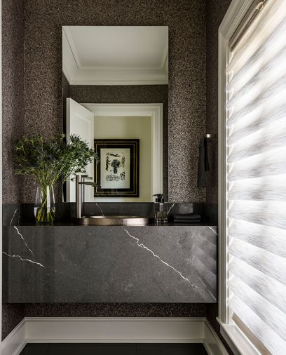 In the powder room, a waterfall slab of Astoria Skys from Elemar and a Hibiscus Hammered Nickel sink by Native Trails from Seattle Interiors, forms the floating vanity. The wallcovering is Granite II from Phillip Jeffries.