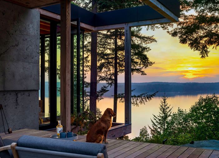 Siena, the dog, takes a moment to enjoy the spectacular sunset view from this tree-filled lot. Locally sourced timber, pivoting doors, and an open framework between the interior and exterior provide an unfettered connection between the kitchen, deck, and the photogenic surroundings.