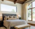 In the primary bedroom, the ceiling has tongue and groove cedar with glulam beams from Miller Lumber by Norman Building & Design. Legum Design added luxe fabrics and furnishings, including the leather bed, wool rug, and velvet bench.
