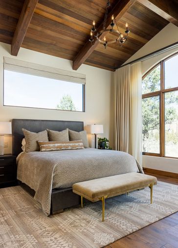 In the primary bedroom, the ceiling has tongue and groove cedar with glulam beams from Miller Lumber by Norman Building & Design. Legum Design added luxe fabrics and furnishings, including the leather bed, wool rug, and velvet bench.