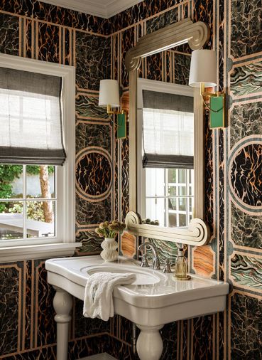 An existing vintage powder room sink gets star treatment set against a Gucci marble print wallcovering. The Art Deco style Tennyson Mirror is flanked by a pair of Hockney Sconces from Urban Electric Co. that echo the wallcovering’s array of color.