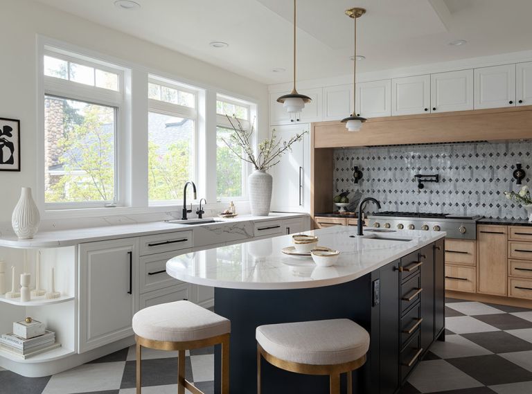 Checkered CLING Industrial Vinyl Tile flooring expands this large kitchen, highlighting cabinetry by Crystal Cabinet Works, Titanium Gold Leather and Unique Calacatta Vagli counters from Architectural Surfaces, and an elegant Daltile backsplash that mirrors the flooring. A dash of Sherwin Williams paint, island Hudson Valley pendants and sconces from Peared Creations brighten the room. Uttermost Ivanna counter stools finish off the look.