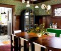 In the dining room, an Archival William Morris Wallpaper in the pattern “Blackthorn in Green” from Zoffany-Sanderson Wallpapers contrasts with a curved bar cabinet and Trapeze 7 Mobile Light from Apparatus Lighting.