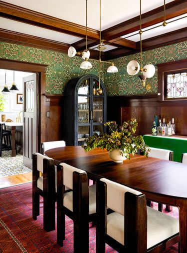 In the dining room, an Archival William Morris Wallpaper in the pattern “Blackthorn in Green” from Zoffany-Sanderson Wallpapers contrasts with a curved bar cabinet and Trapeze 7 Mobile Light from Apparatus Lighting.