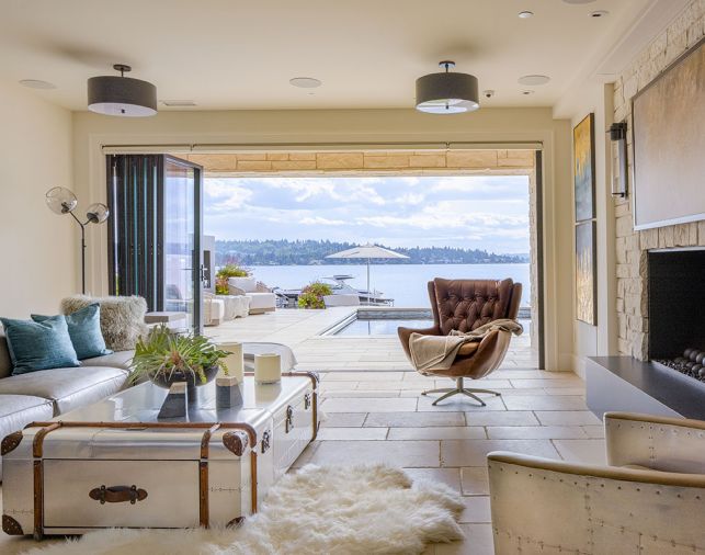 The small former dining room becomes a lounge featuring four RH Reginald Leather Swivels cozying around a CB2 Darbuka Coffee Table. The soaring two-sided fireplace with metal surround echoes Antique Pearl stone found on exterior. A McEwen Prism Extension Fixture from Trammel Gagné pops against custom oak ceiling panels.