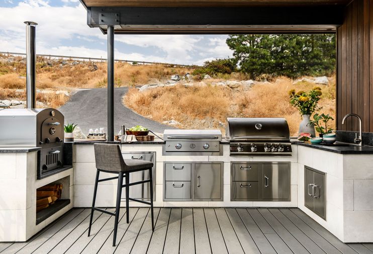 ABOVE The outdoor kitchen is well-equipped, complete with a Tuscan Chef wood-fired pizza oven, Le Griddle, and Blaze Grill, all from from BBQGuys. A granite counter surrounds an Elkay sink and Lynx Grills faucet from Ferguson
