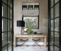 Marble covers the entry floor and a candle-style chandelier lights the way. The leather stools, desk, oversized mirror, and elegant Phillip Jeffries wallcovering are welcoming.