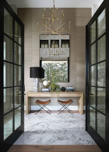 Marble covers the entry floor and a candle-style chandelier lights the way. The leather stools, desk, oversized mirror, and elegant Phillip Jeffries wallcovering are welcoming.