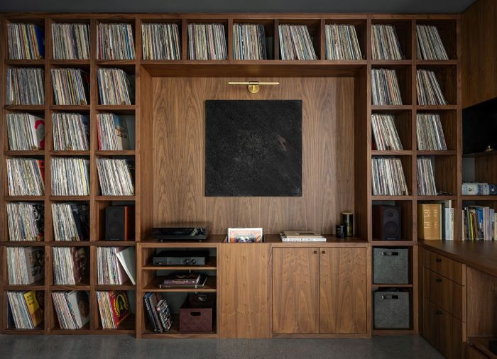 Walnut shelving and cabinetry in the office is crafted by Northwest Custom Cabinets, to house the homeowner’s extensive record collection. A brass RH sconce highlights artwork by Erin Sullivan.