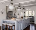 The expansive kitchen island has cabinetry by Northwest Custom Cabinets painted in Sherwin Williams “SW Cadet” and features Classic Brass hardware. The Infinity White Quartzite honed counter and matching backsplash are lit by pendant lighting.