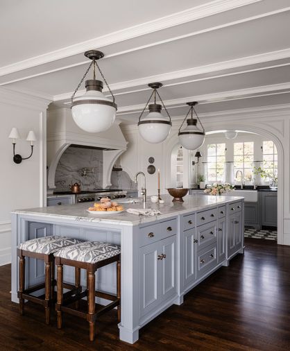The expansive kitchen island has cabinetry by Northwest Custom Cabinets painted in Sherwin Williams “SW Cadet” and features Classic Brass hardware. The Infinity White Quartzite honed counter and matching backsplash are lit by pendant lighting.