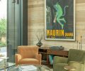 The lounge has a framed 1920s vintage advertisement poster hanging above the custom sideboard. Four Maiden Home armchairs, each in a different color, surround a Timothy Oulton coffee table and all sit atop layered rugs from Lulu and Georgia.