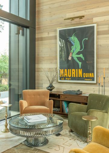The lounge has a framed 1920s vintage advertisement poster hanging above the custom sideboard. Four Maiden Home armchairs, each in a different color, surround a Timothy Oulton coffee table and all sit atop layered rugs from Lulu and Georgia.