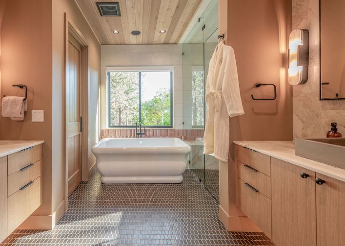 Various natural materials were combined for a welcoming primary bathroom, including fluted lapidary tile from Clé that adds depth behind the freestanding tub and continues into the shower. The wood ceiling syncs with the rift white oak cabinetry and Ann Sacks floor tile.