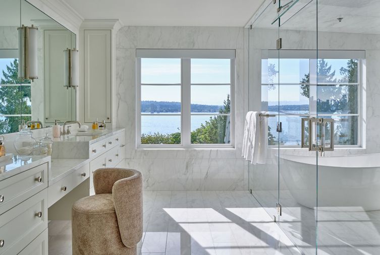 The completely redesigned primary bath glows with exquisite slabs of flow-matched Calacatta Caldia marble honed across every surface. Custom floating dual vanities by Barneswood Custom Cabinets with makeup chair offer views of Lake Washington.