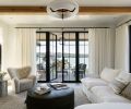 White plaster walls, gauzy white sheers, and mullioned black windows all cluster around a Nickey Kehoe green leather hassock, cushy chaise sofa and Audo Copenhagen chair.