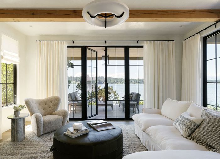 White plaster walls, gauzy white sheers, and mullioned black windows all cluster around a Nickey Kehoe green leather hassock, cushy chaise sofa and Audo Copenhagen chair.