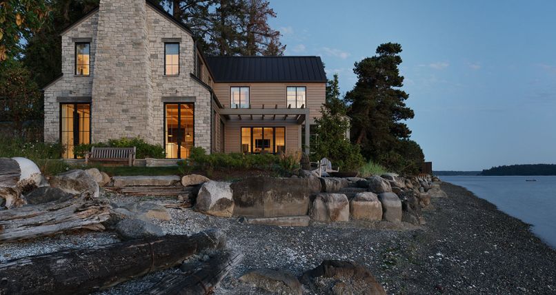 Seen at night against the peninsula’s calm waters, 100-year-old trees are an elegant backdrop, along with the rocky landscape. The home’s limestone glows in the moonlight, while Western red cedar siding and standing seam roof frames the structure.