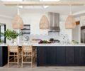 An oak island with custom ebony dye and quartz countertop pops against Benjamin Moore’s “Simply White” walls. Custom cabinetry throughout by Juggernaut Woodworking. Serena & Lily rattan pendants suspended below the wagon-wheel skylight echo teak and rattan stools below.