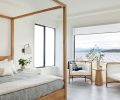 The swivel milk glass sconce is handy for reading in the reclaimed French oak four-poster bed. In order to keep the primary suite cozy day or night, motorized roller shades were installed from Window Fashions Northwest.