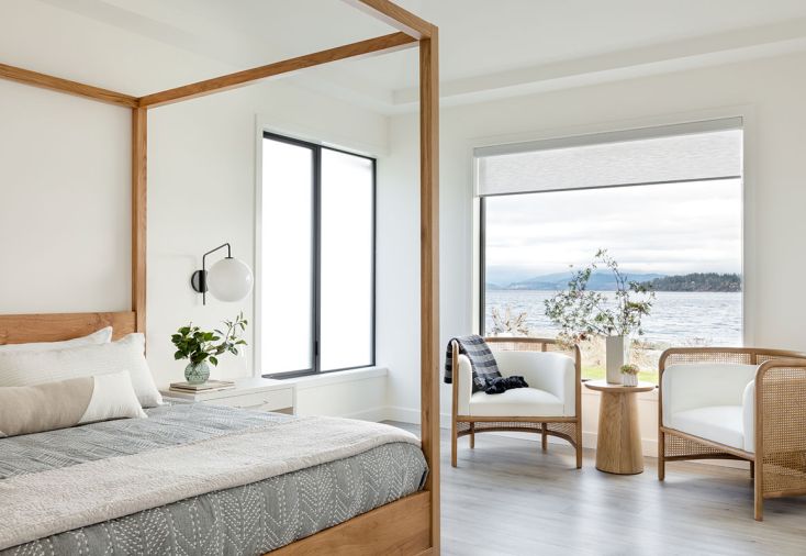 The swivel milk glass sconce is handy for reading in the reclaimed French oak four-poster bed. In order to keep the primary suite cozy day or night, motorized roller shades were installed from Window Fashions Northwest.