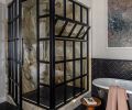 A custom glass shower enclosure from Dyna Metal is paired with Calacatta Gold shower walls, marble floors, and marble and brass tile wainscot in the primary bathroom.