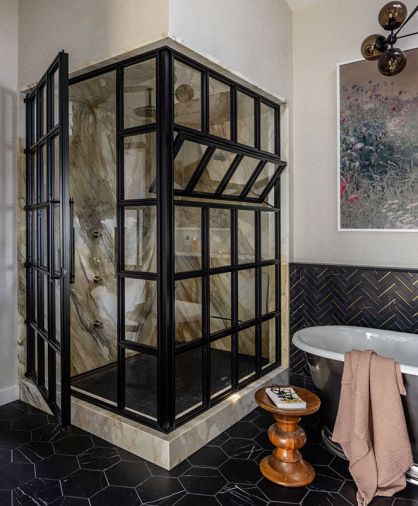 A custom glass shower enclosure from Dyna Metal is paired with Calacatta Gold shower walls, marble floors, and marble and brass tile wainscot in the primary bathroom.