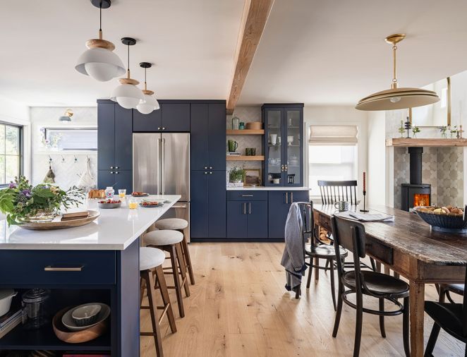 The far wall provides an array of storage, from wall hooks to pantry cabinets surrounding the refrigerator, to a serving alcove with open shelves and dishware displayed behind glass doors.