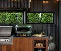 Custom Ipe cabinet fronts are sleek and durable, with niches for kindling to fire up the dual-fuel Gozney Dome Outdoor Pizza Oven, and hidden grill utensil storage. The concrete flooring leads to the exterior deck via a sliding Fleetwood Door System.