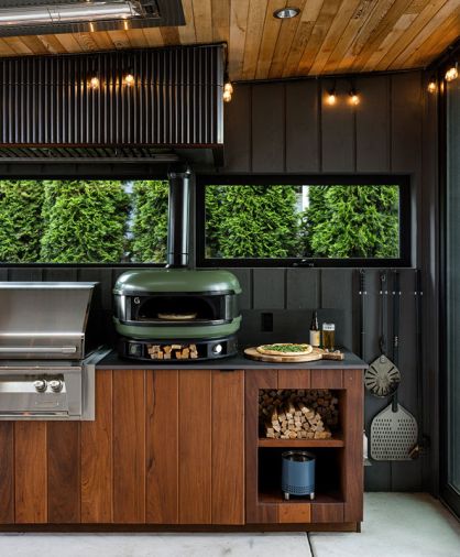 Custom Ipe cabinet fronts are sleek and durable, with niches for kindling to fire up the dual-fuel Gozney Dome Outdoor Pizza Oven, and hidden grill utensil storage. The concrete flooring leads to the exterior deck via a sliding Fleetwood Door System.