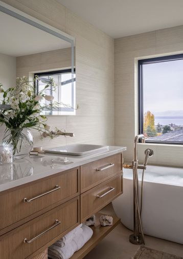 This powder room is a surprise reveal to guests, thanks to a dramatic black-and-white palette, via Thibaut black grass cloth wallcovering, MSI marble, and a black vanity by Thompson Traders with Palmer Industries. A touch of paint and glossy plumbing fixtures by Brizo add to the elegance. Sculptural accents, such as the DMF and Alora Lighting and a uniquely shaped mirror, offer unexpected movement.