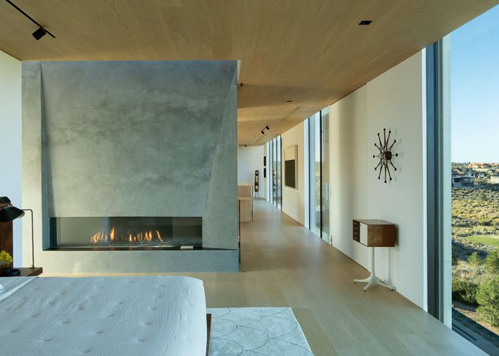 The primary suite can be closed off for privacy by a large (unseen) pivot door. The central fireplace rises into the suite with a silvery plasterwork finish. Artworks adorning the walkway to guest bedrooms include Louise Nevelson and Richard Serra. Slab bed by BDDW.