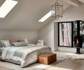 The guest suite has rugs from Armadillo in front of a freestanding Rais stove and large picture windows with views into the trees. The chandelier sourced from Ay illuminate hangs over a custom bedframe placed beside a vintage bedside table.