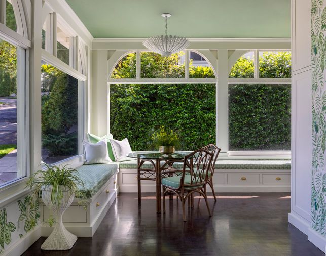 Custom window seats in the sunroom were designed by Nifelle Design and built by Northwest Heritage Renovations, with a vintage bamboo rattan Brown Jordan table and chairs, and Hampton Large Chandelier from Visual Comfort.