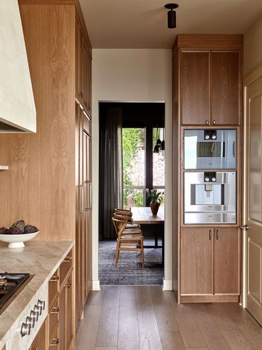 The intimate dining room tempts guests away from the bright kitchen with a moody color palette grounded in Kravet window coverings and the deep warm gray of the ‘Urbane Bronze’ plasterwork.