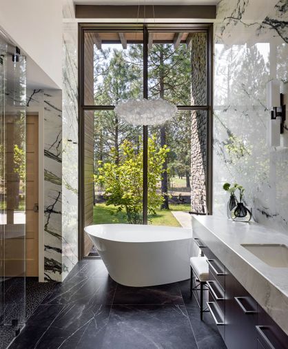 In the primary bathroom, the Modern Forms Fluffy Pendant hangs above the Veil Freestanding Soaking Bathtub by Kohler. Elegant flooring is Boulder Negro Marquina Tile by Porcelanosa.