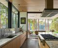 The kitchen opens seamlessly to the outdoors, where a patio serves as a second living room. Cedar ceilings complement views of the lake. Plumbing fixtures throughout were sourced from Best Plumbing.