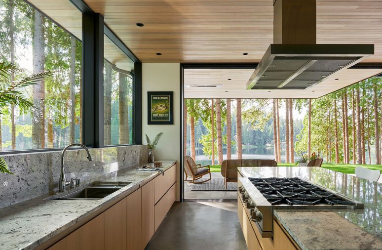 The kitchen opens seamlessly to the outdoors, where a patio serves as a second living room. Cedar ceilings complement views of the lake. Plumbing fixtures throughout were sourced from Best Plumbing.