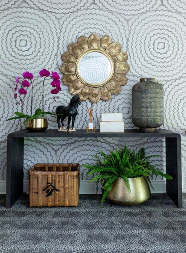 On the stair landing, the walls have Schumacher wallpaper, with a Made Goods console table and a mirror composed of ornate feathers in polished brass from Global Views.