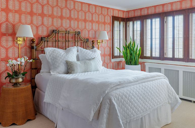 Walls are covered in “Coral Palm Fronds” from Serena & Lily in the guest room. An organic vintage side table and bamboo headboard are balanced with brass swing arm sconces.