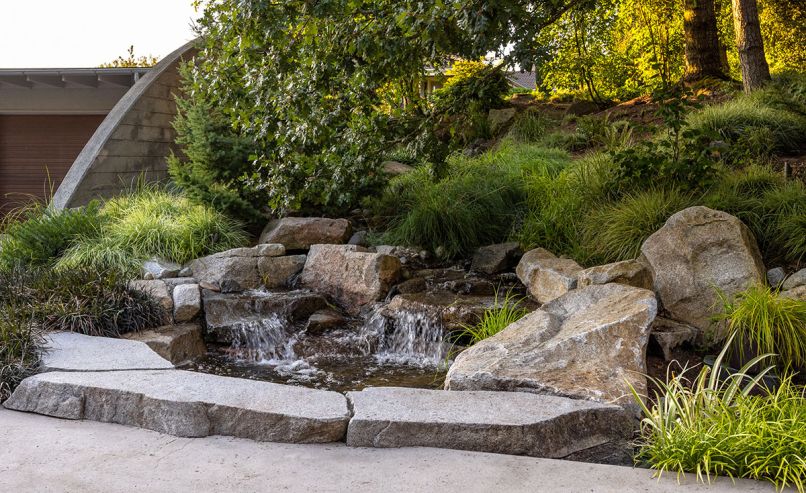 The water feature that abuts the driveway is one of two located adjacent to the south deck. Turnstone Construction utilized Weathered High Cascade Granite to create the peace-making waterfall.