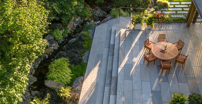 Holsapple turned a former circular deck with railing into a larger square one using Grey Sandstone and adding steps to each side. Sutherland teak table and chairs from Terris Draheim Outdoor. Plantings include Irish and Scotch Moss.