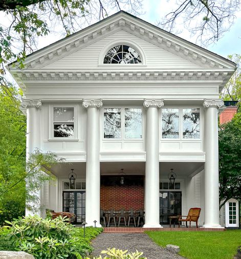 A classic fan light window crowns four massive Ionic columns restored by Arciform. The brick chimney is flanked by two pairs of restored French doors on the side porch.