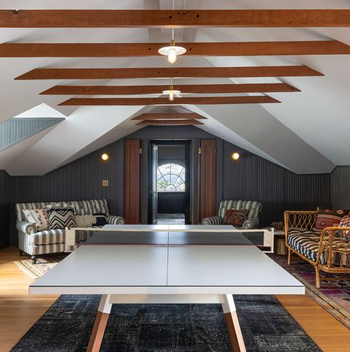 An expanded play area replete with ping pong table features a vaulted ceiling that exposes the collar ties for further panache as well as two sofas to sprawl on.